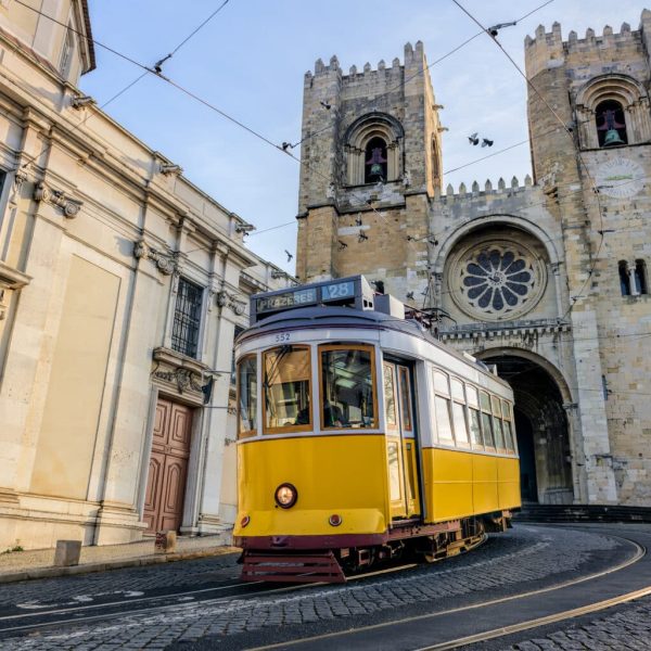 A famous yellow tram 28 passing in front of Santa Maria cathedral in Lisbon, Portugal